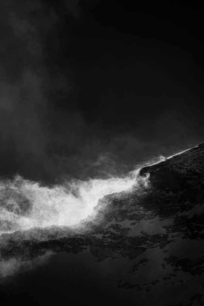 Captivating black and white image of a snowy mountain peak with dramatic lighting and mist.